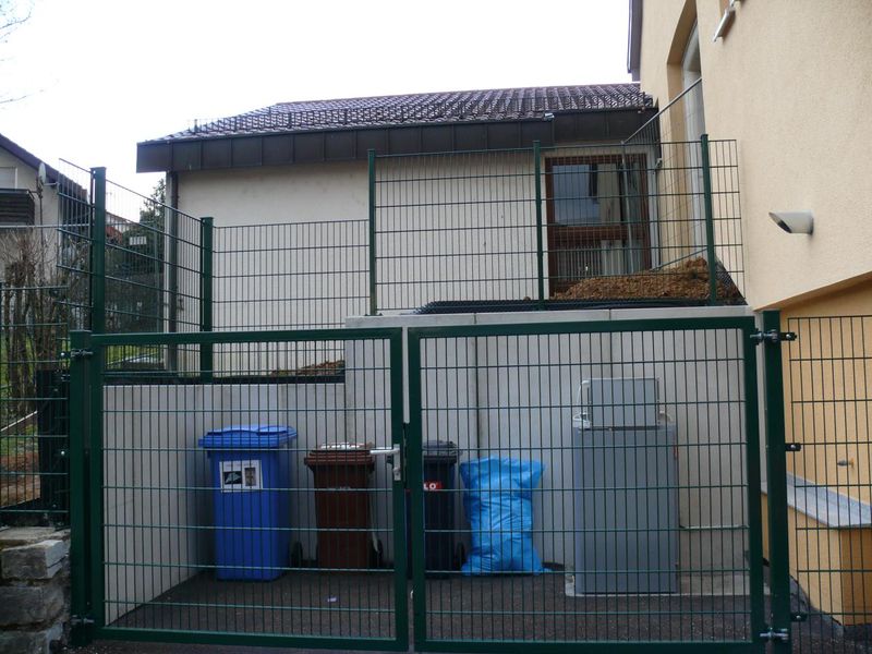 Grün beschichtete Einhausung mit Tor aus Doppelstabmatten an der Entsorgungsstation eines Kindergartens